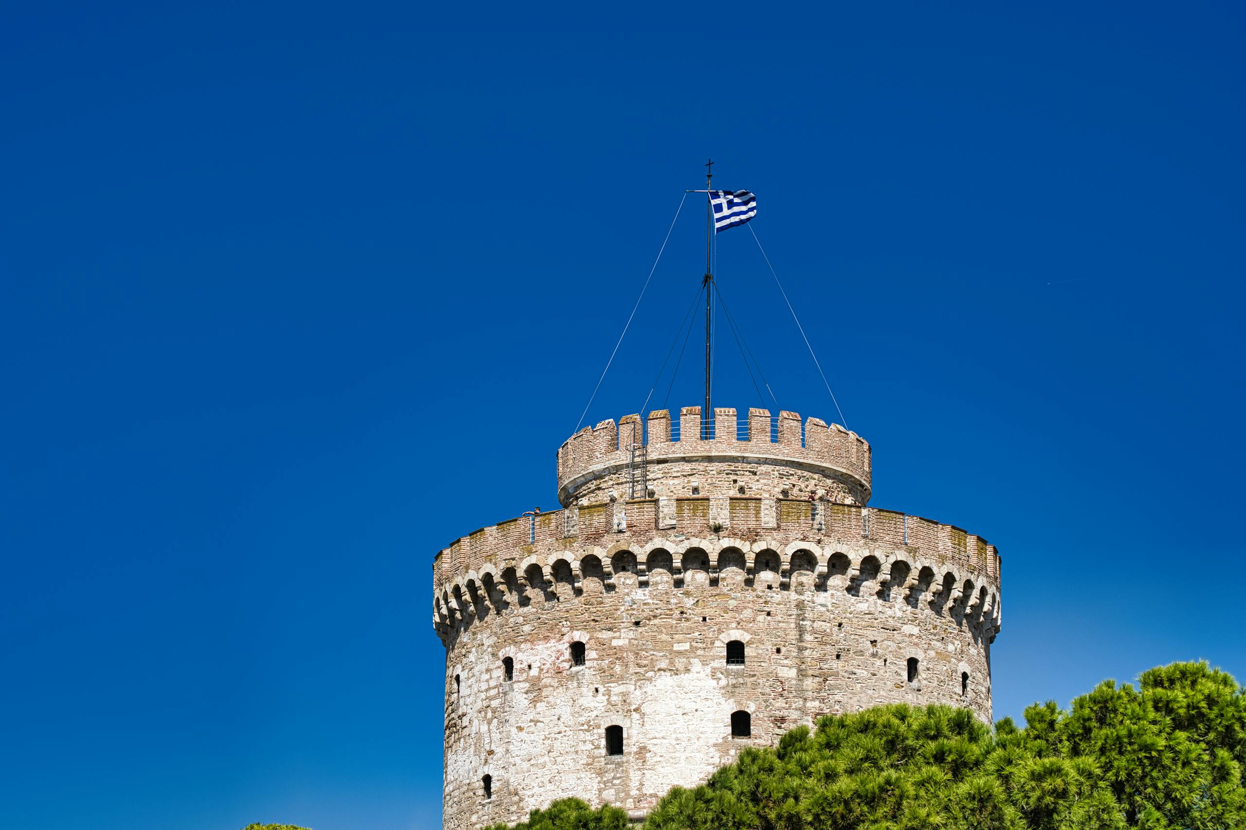 À la découverte des Monuments et de la Culture de Thessalonique 3 Majestic view of the historic White Tower of Thessaloniki against a bright blue sky with a Greek flag.